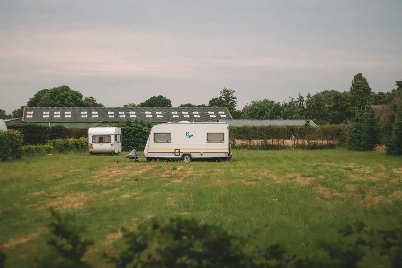 Campingvogne på en grøn plads foran en gård